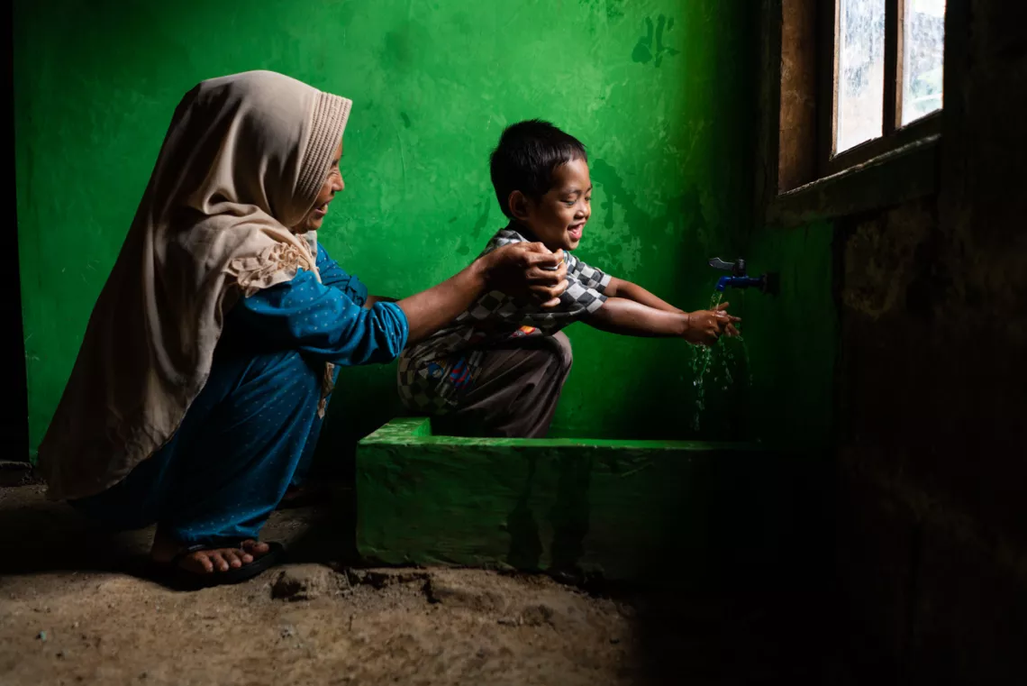 Wahyu watches her son Rizki, 4, wash his face in a newly built clean water and sanitation facility