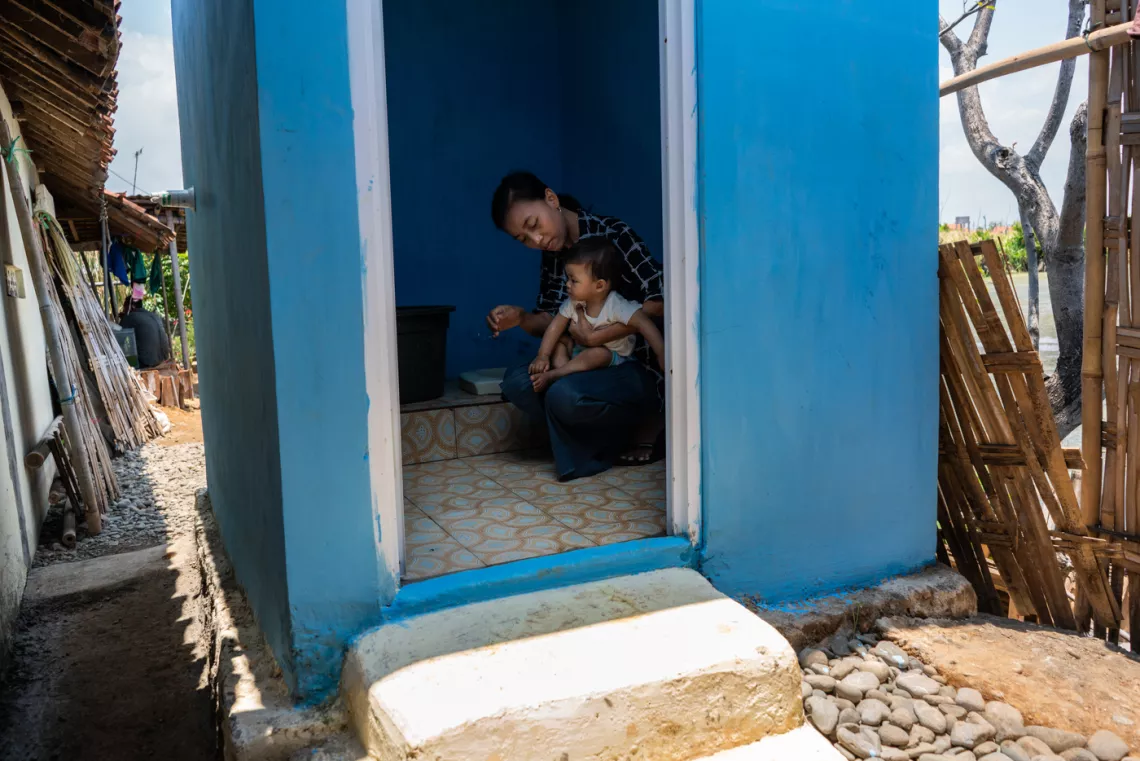 Hanifah holds her 11-month-old daughter Dinda in a newly constructed toilet outside their home.