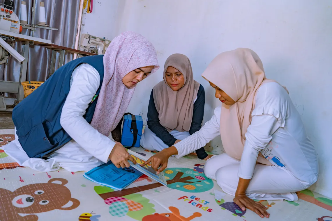 Marlina (left), immunization coordinator and vaccinator at Padang Tiji Community Health Centre (Puskesmas), and her colleague (right) talk to Dahniar (centre) about child immunization. Pidie Regency, Aceh Province, Indonesia. 