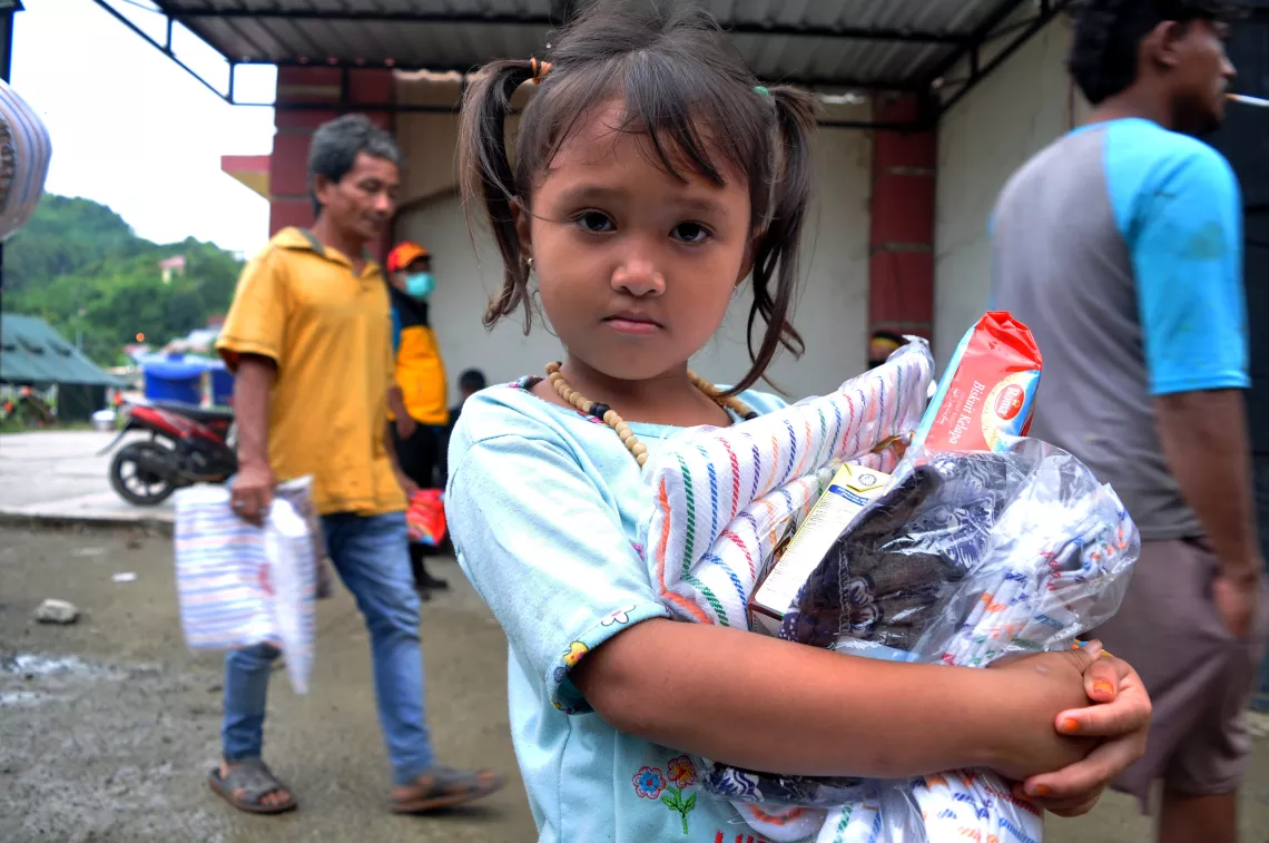 Tima, 5, carries food and a blanket she received from an aid distribution at a shelter at Manakarra Stadium in Mamuju Regency, West Sulawesi, Indonesia, on 17 January 2020.