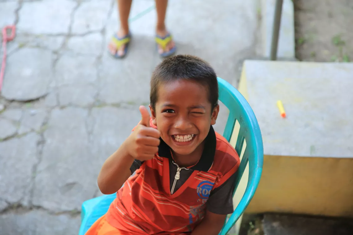 A young boy winking and showing thumbs up.