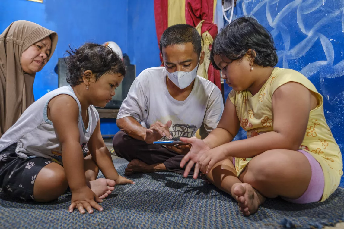 Afiqa (right) watches a video of her mother on her father&rsquo;s phone.