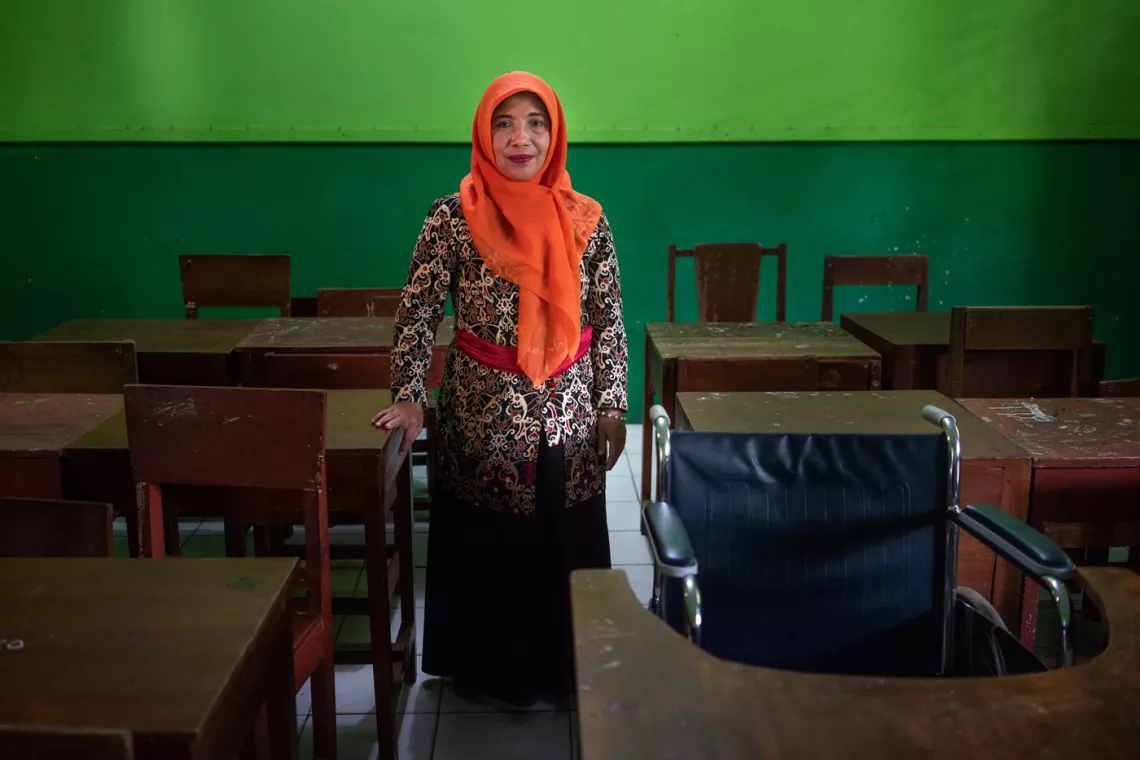 Ibu Darsiti berdiri di samping kursi roda yang ia telah usahakan untuk Syaiful