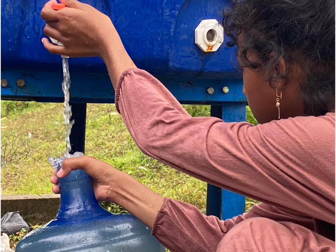 Kino, 11, helps her sibling collect water in a used gallon jug. After an earthquake hit, Kino&rsquo;s family has limited access to water, forcing them to find water wherever they can.