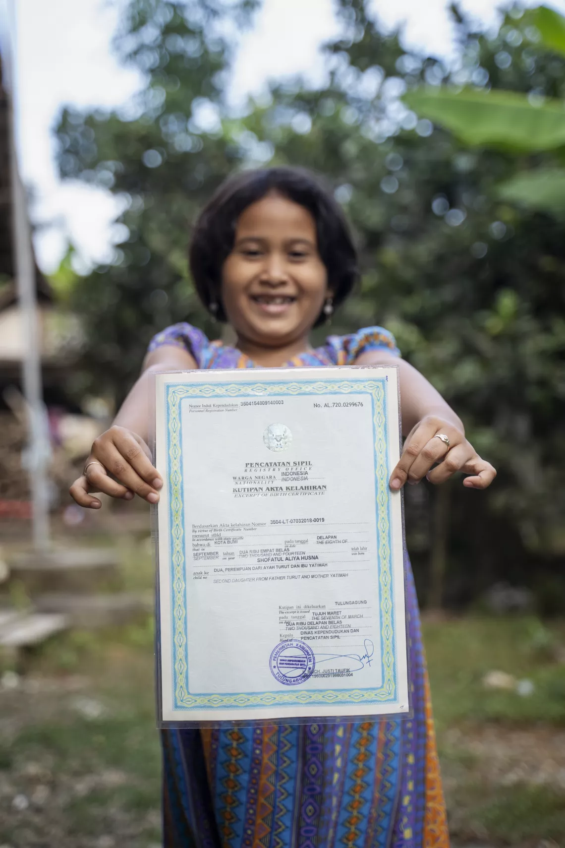 Alia menunjukkan akta kelahirannya, dibarengi oleh orang tuanya. 