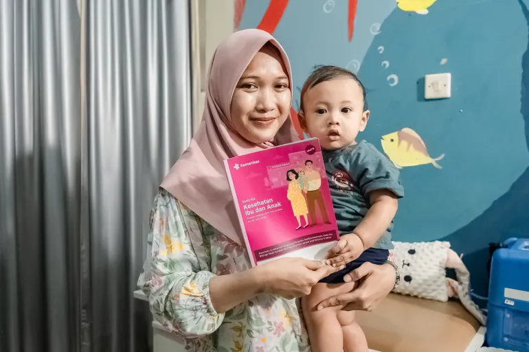 A mother holding her baby and a KIA book