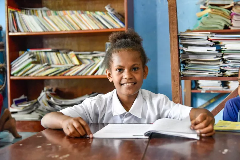 A girl smiling while reading a book in her class