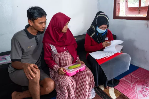 Titis, age 28, who is 37 weeks pregnant, with her husband Sugeng, checks her name on a hand-over form with the puskesmas health cadre after receiving the local-based food supplementation for malnourished pregnant women (PMT lokal ibu hamil) provided by puskesmas health cadres in their home in Kediri, East Java.