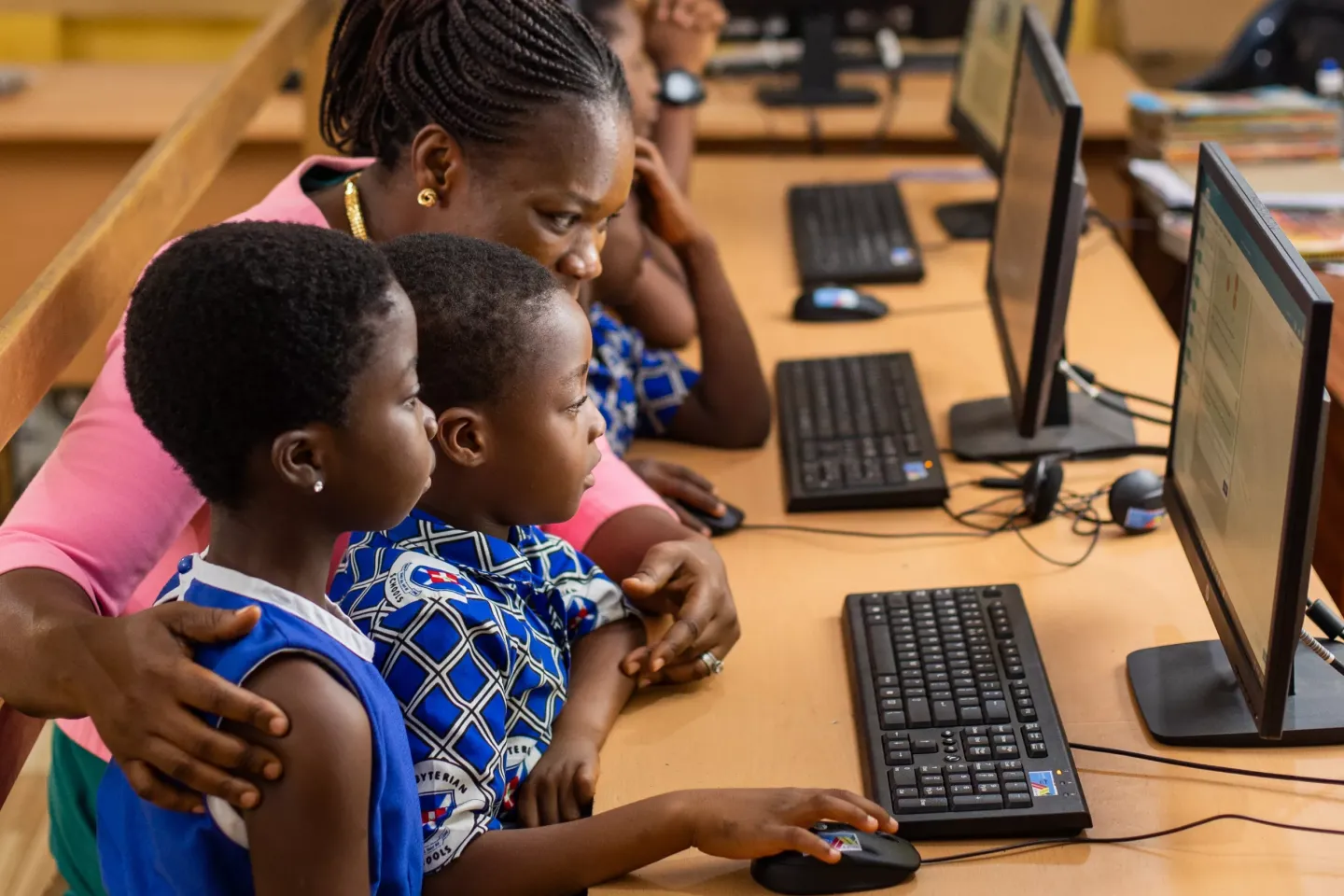 A teacher helps two young children use a computer