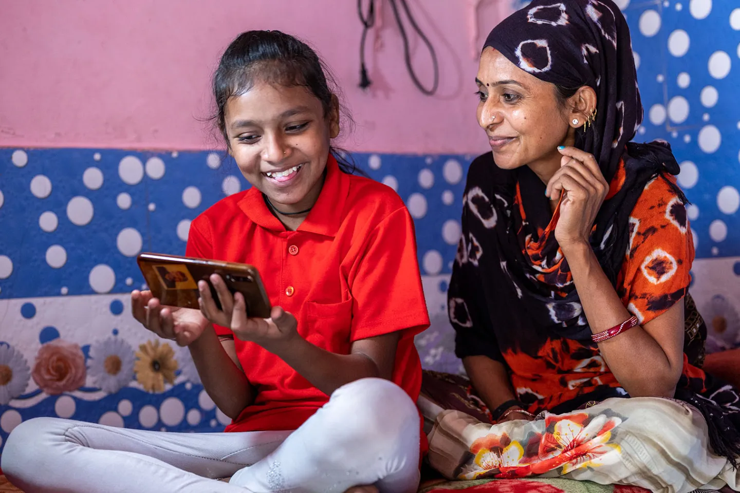 A mother sits next to her daughter who is holding a mobile phone