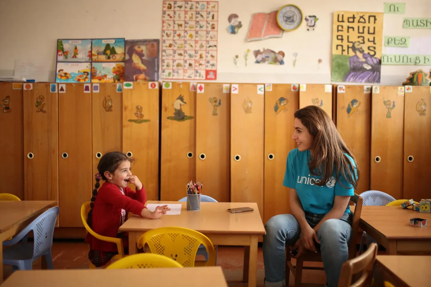UNICEF worker sitting and talking to a young girl in her kindergarten classroom