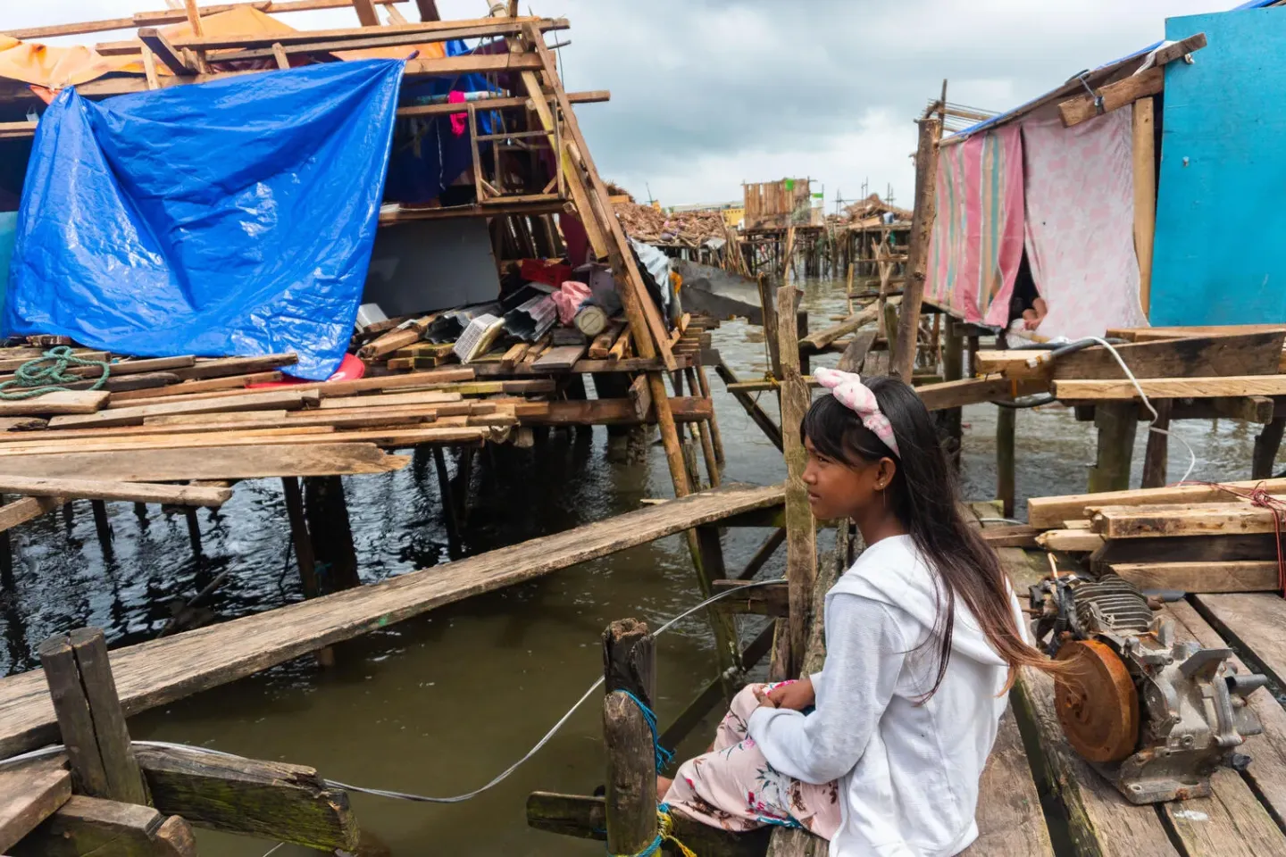 12-year-old child sits on wooden platform amid flooding and destruction from a Typhoon