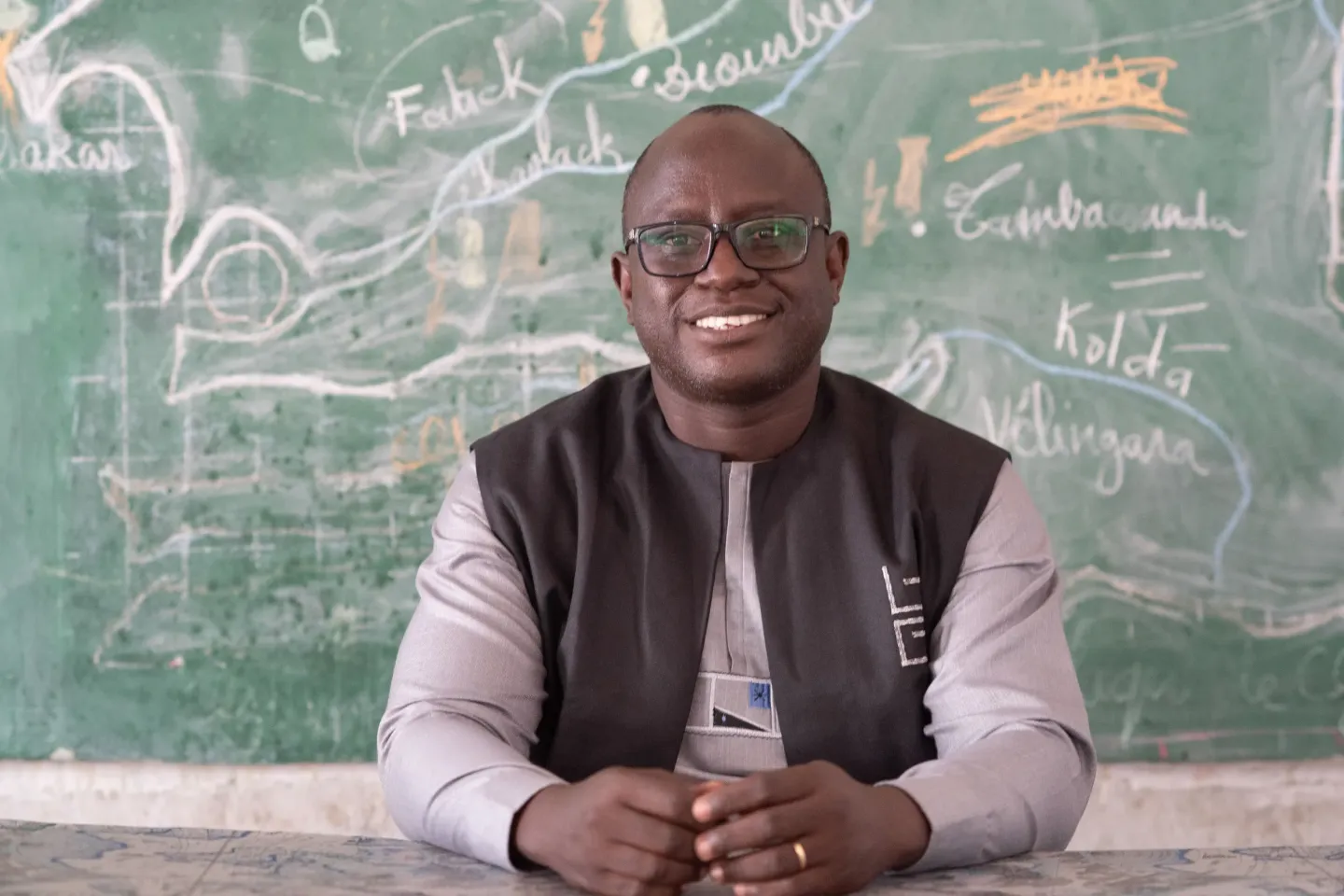A school teacher sits at a desk at the front of their classroom 