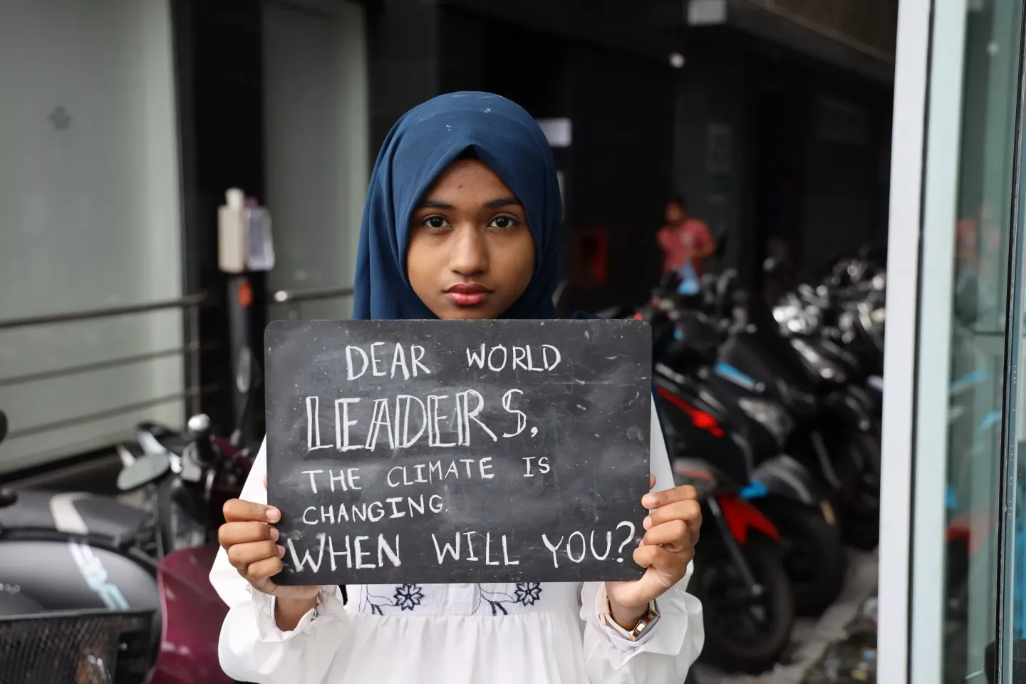 A child holds up a blackboard with a message that says "Dear world leaders, the climate is changing, when will you?"