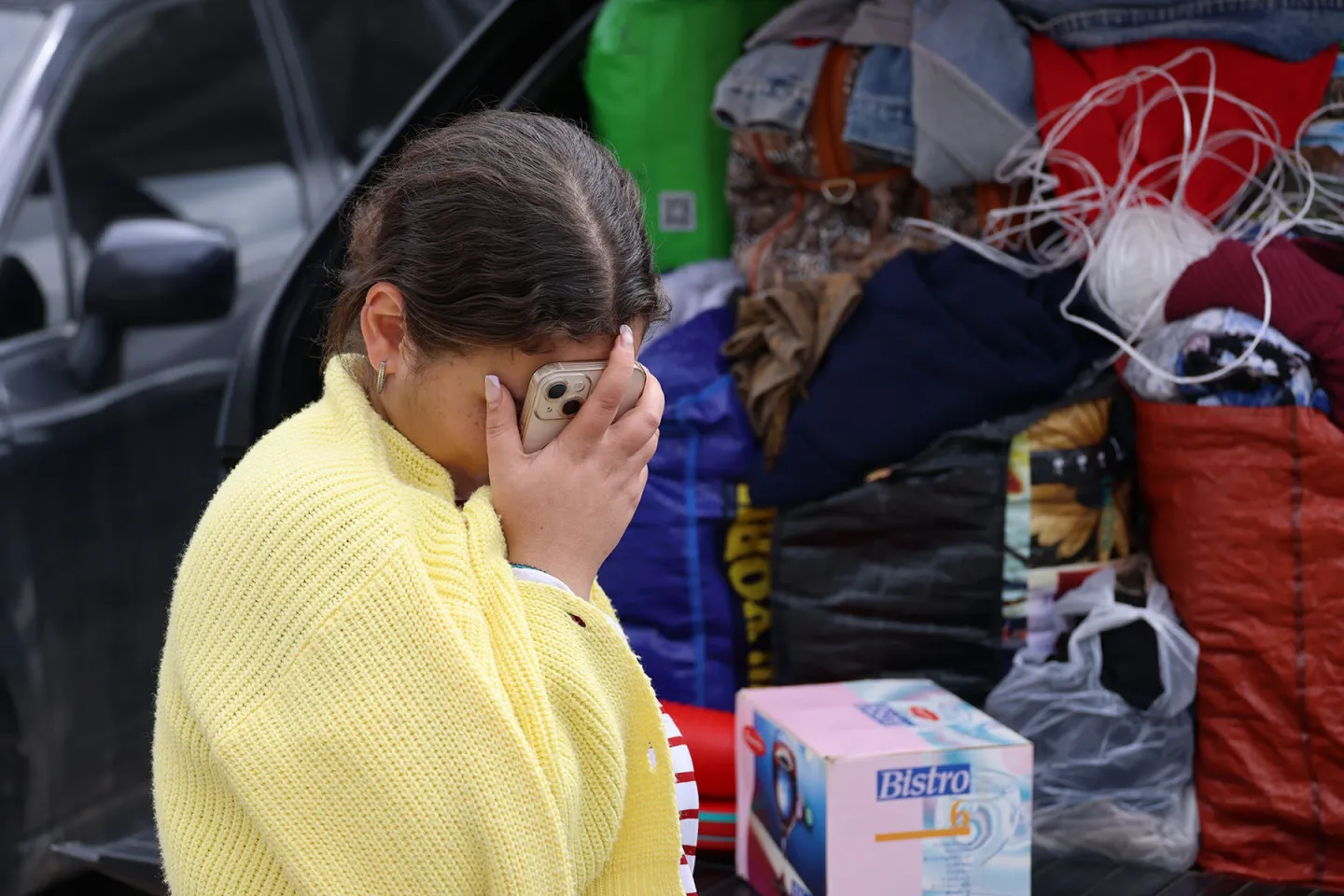 Young refugee woman wearing a yellow sweater holds her head and smartphone in her hand