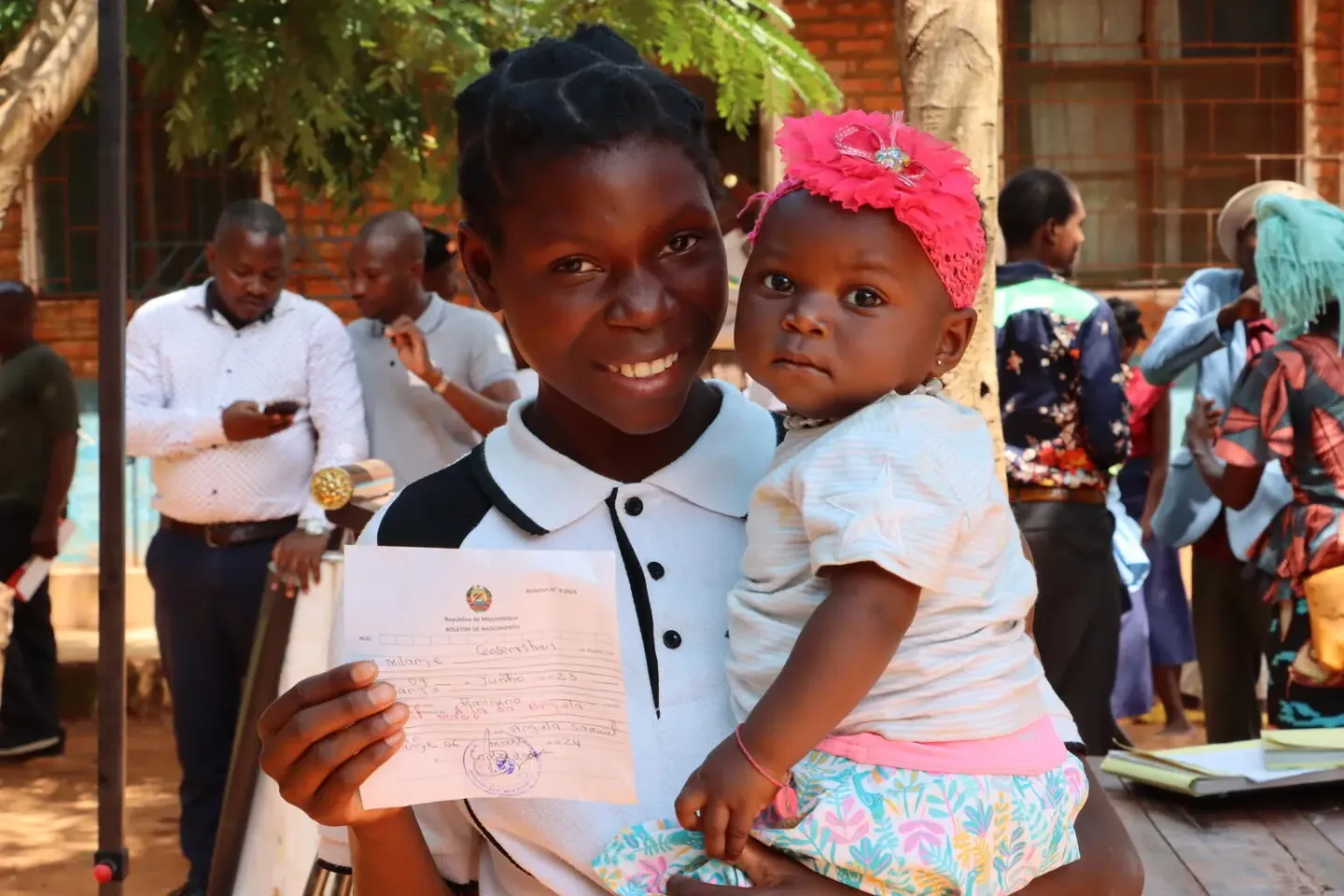Caretaker holds a baby and their new birth registration paper