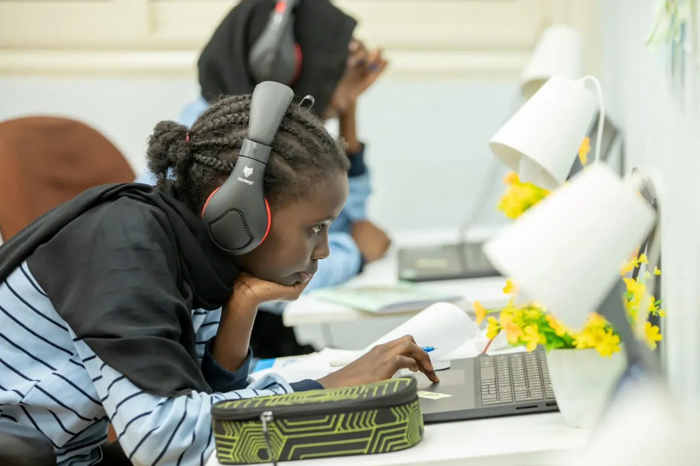 Children wearing headphones and using laptops as a desk.