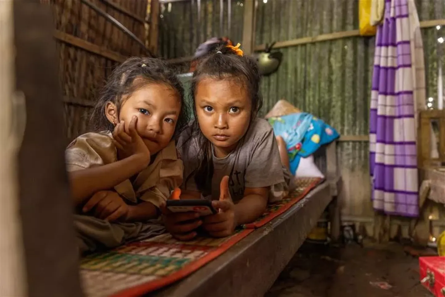 Two young girls looking at the camera while one is holding a phone
