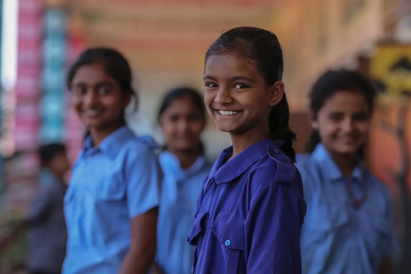 Four young girls smiling at the camera. One is in focus in the foreground, while the others are a little blurred in the background