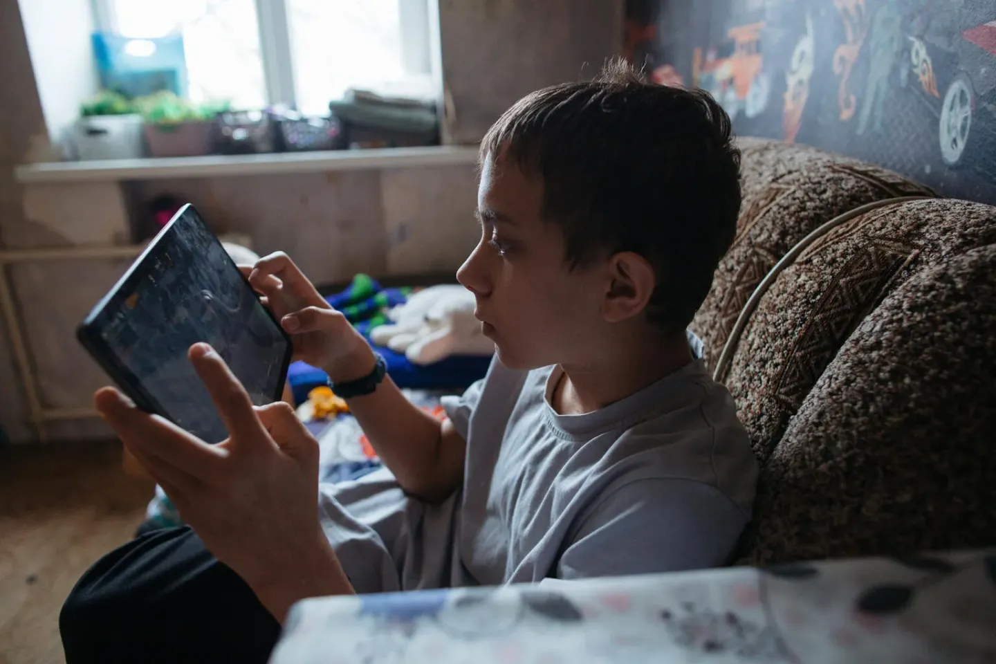 Boy uses a tablet while sitting on a sofa at home