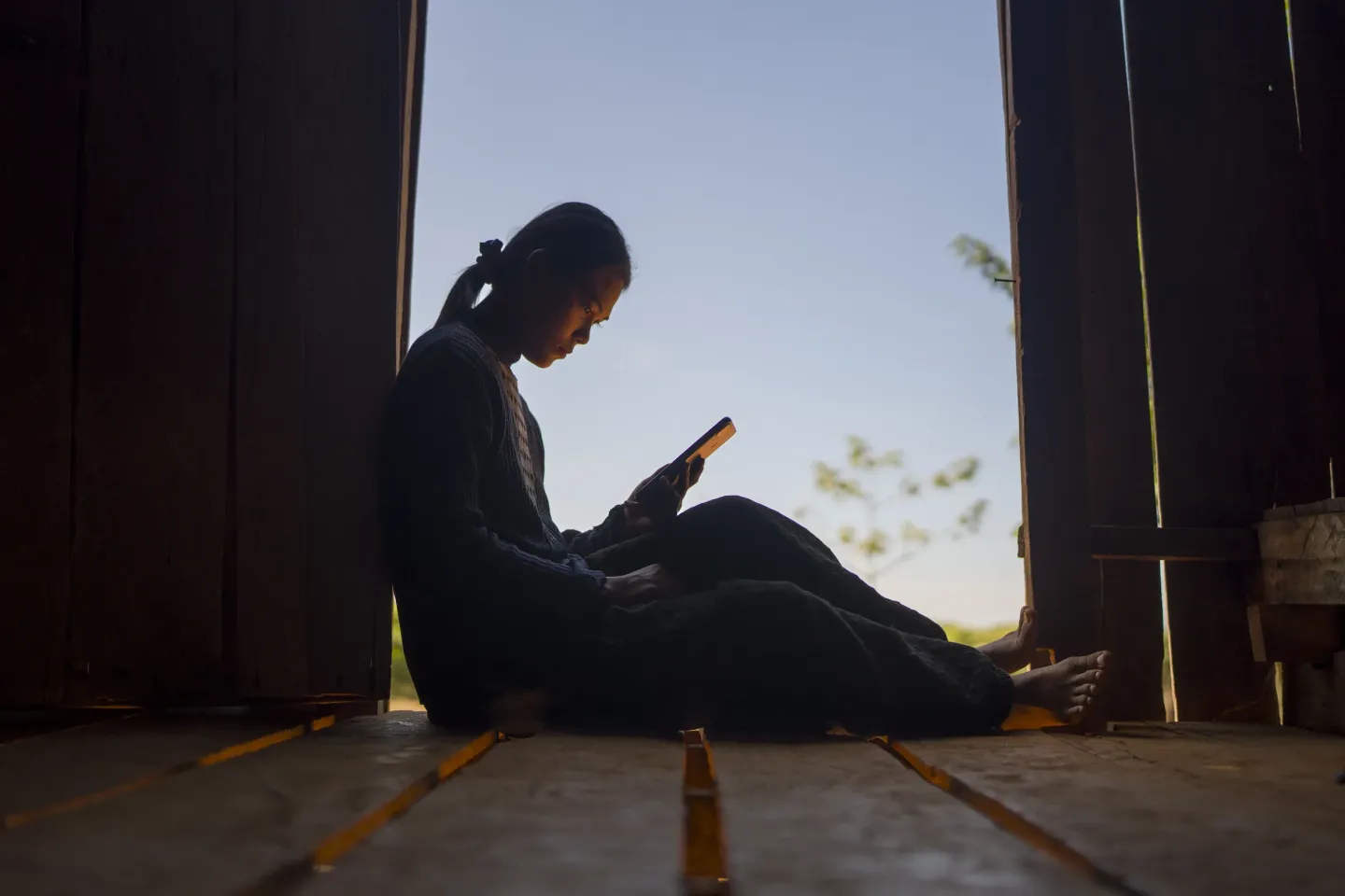 Silhouette of a teenager sitting in a window at home, looking at their smartphone