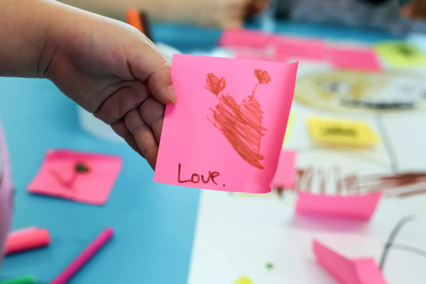 Child from Hamilton East School in New Zealand holding a post-it note that says "love"