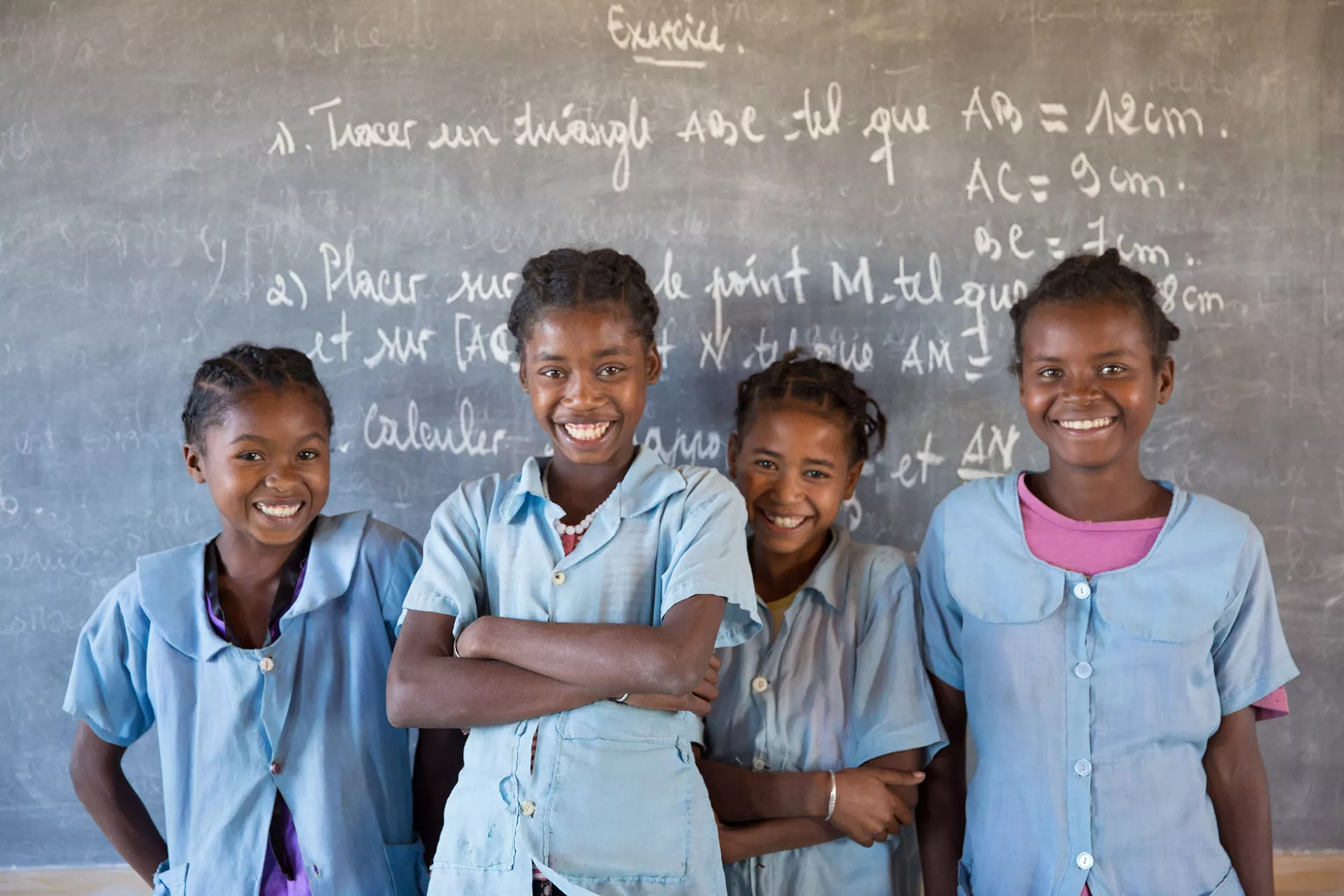 4 school girls stand in front of a black board