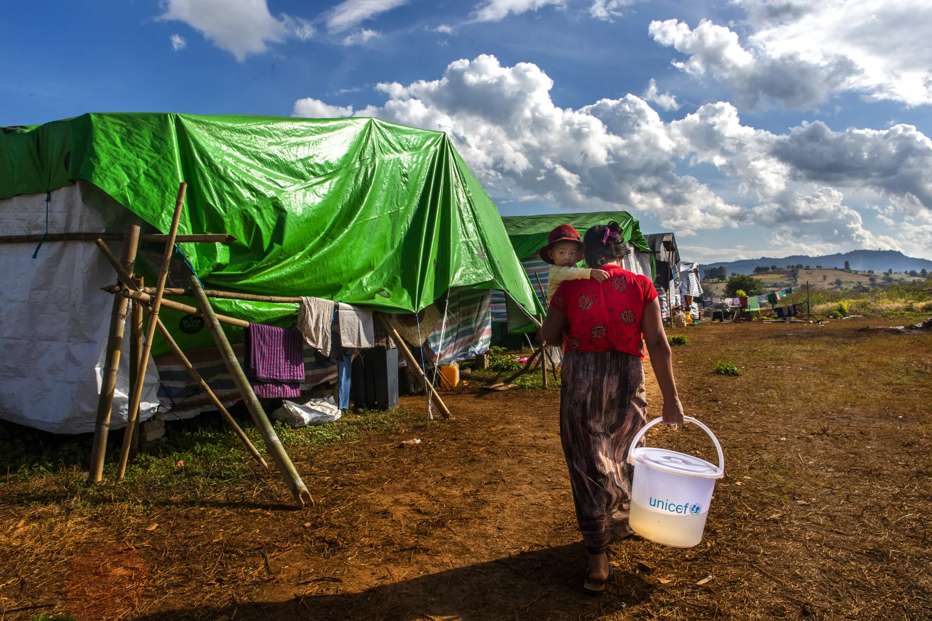 Woman carries a water bucket in one hand and her child in the other