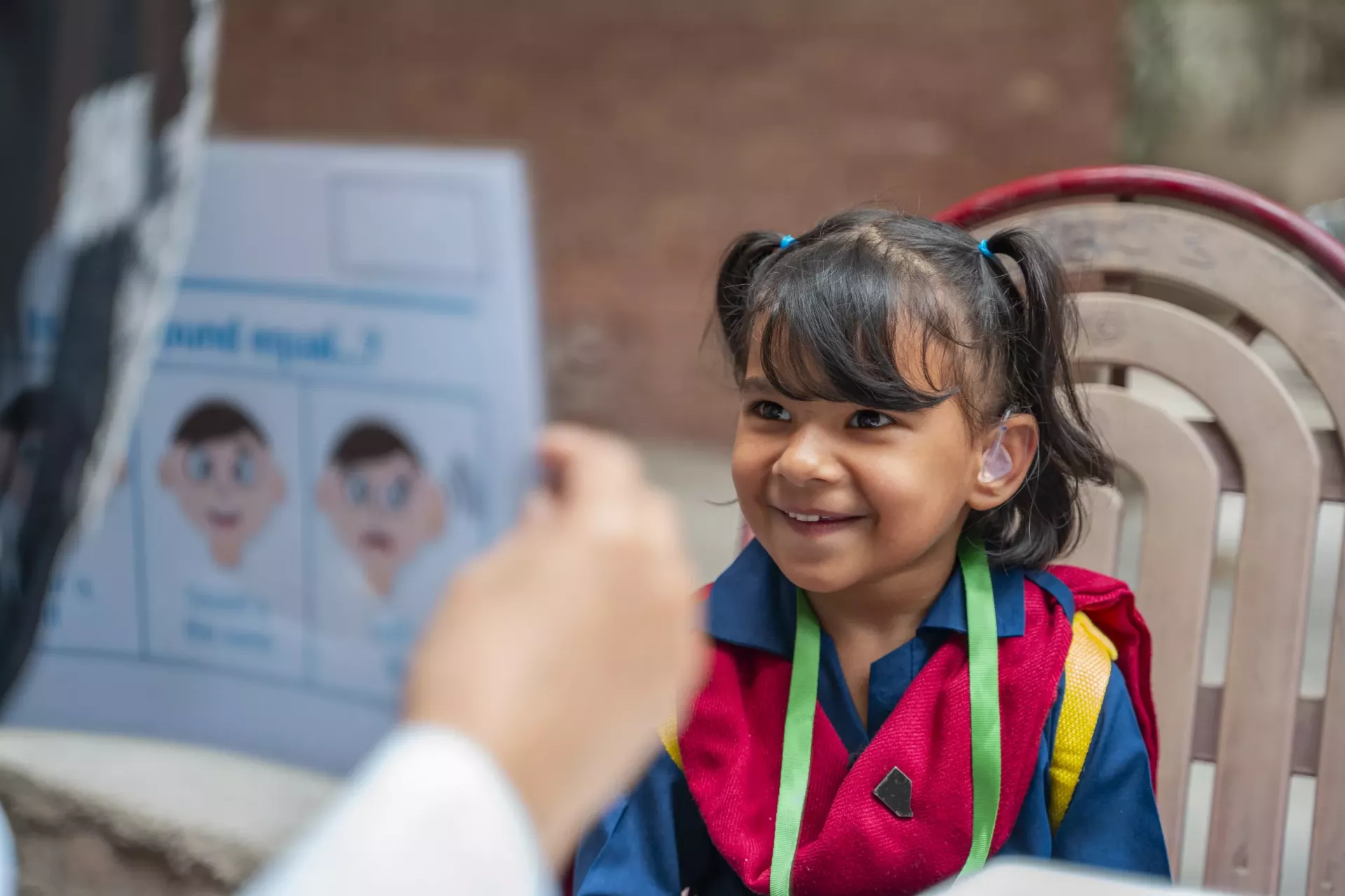 A young girl with a hearing aid smiling as an adult shows her a book