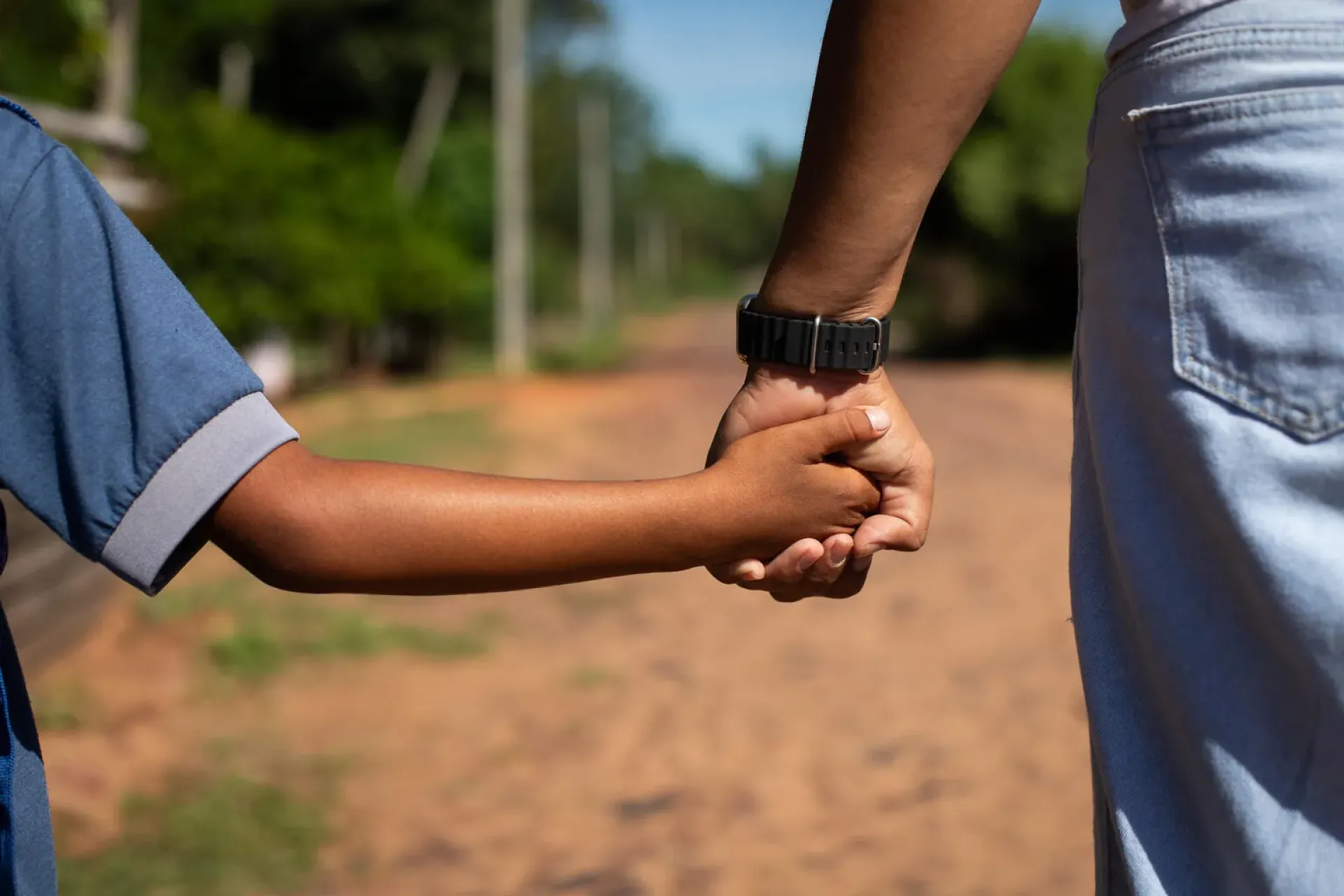 Child and mother holding hands while they walk down a dirt road