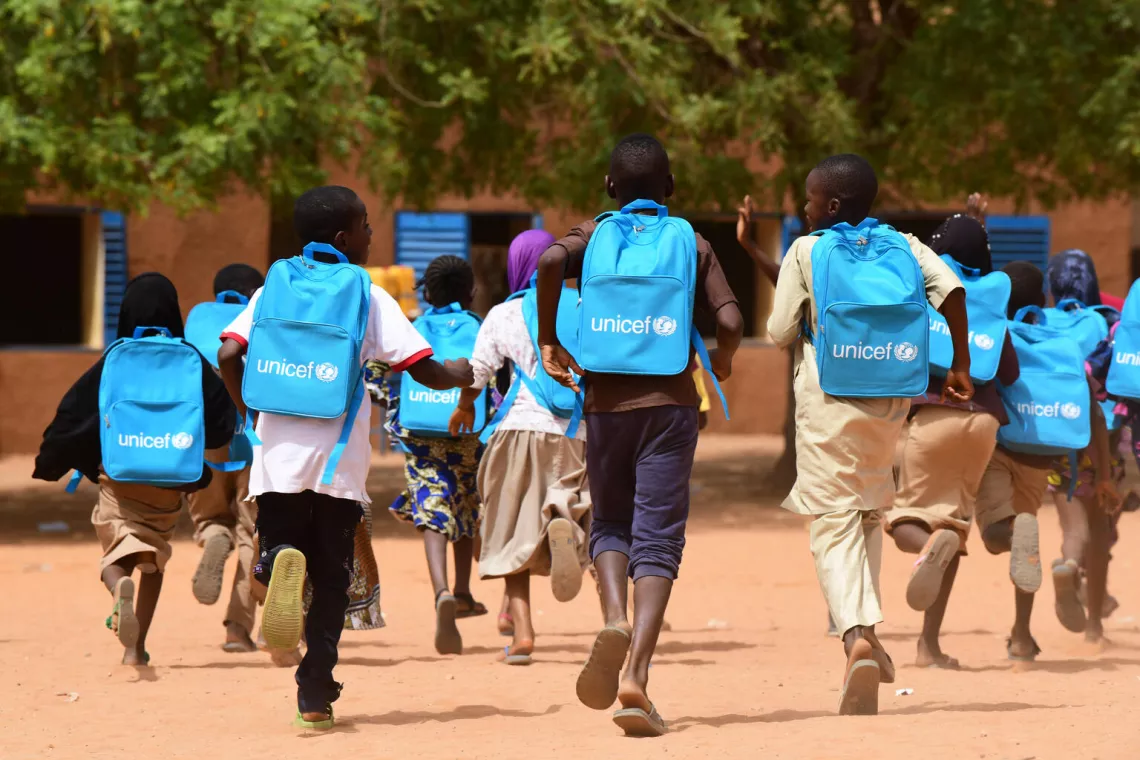 Group of children run wearing UNICEF backpacks.