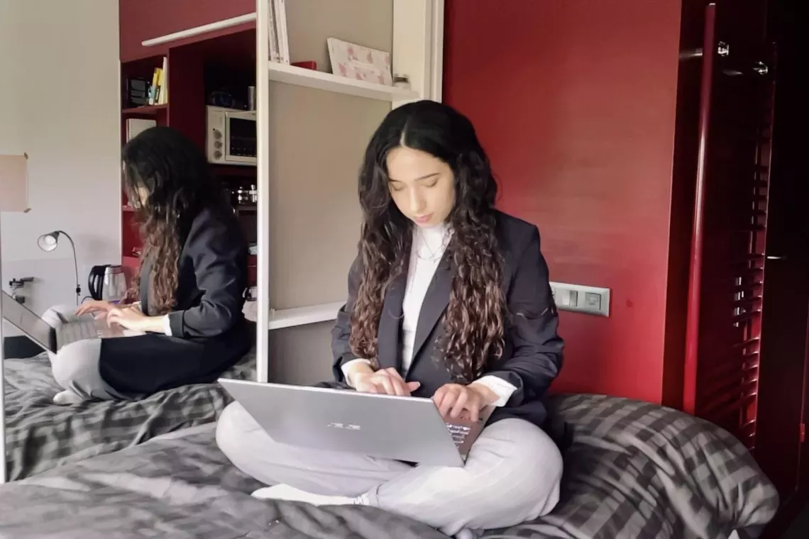 A teenage girl sits on her bed with a laptop on her lap