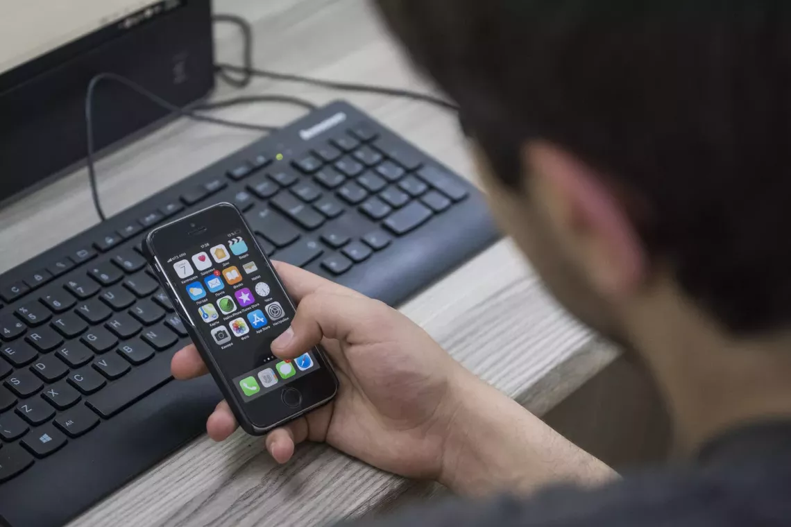 A child seen from behind with a smartphone and a computer