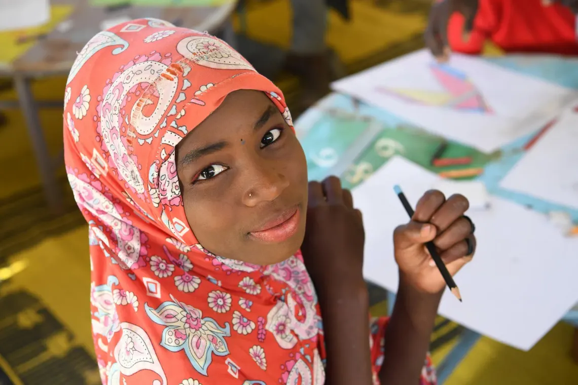 School student turns toward the camera, holding a pencil in her hand