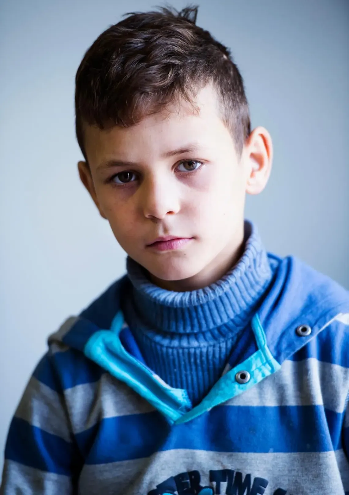 A boy peers into the camera with a neutral expression. 