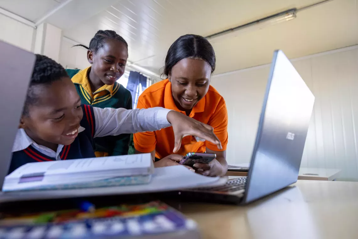 Three children at school, laughing as they use a laptop