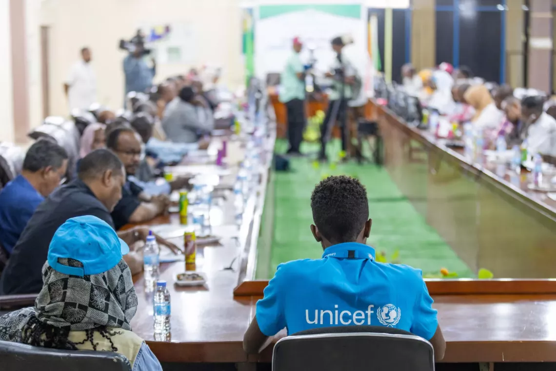 A child wearing a UNICEF shirt at a meeting with adults