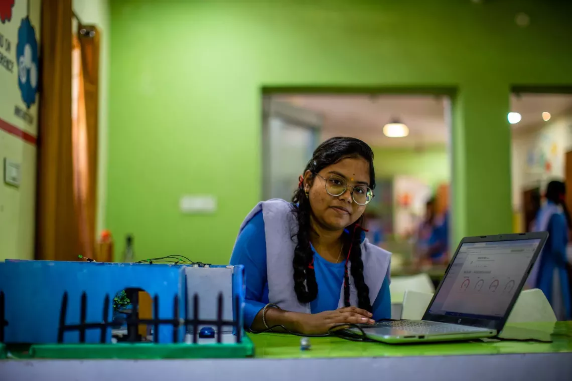 A young girl with a laptop open and looking at the camera