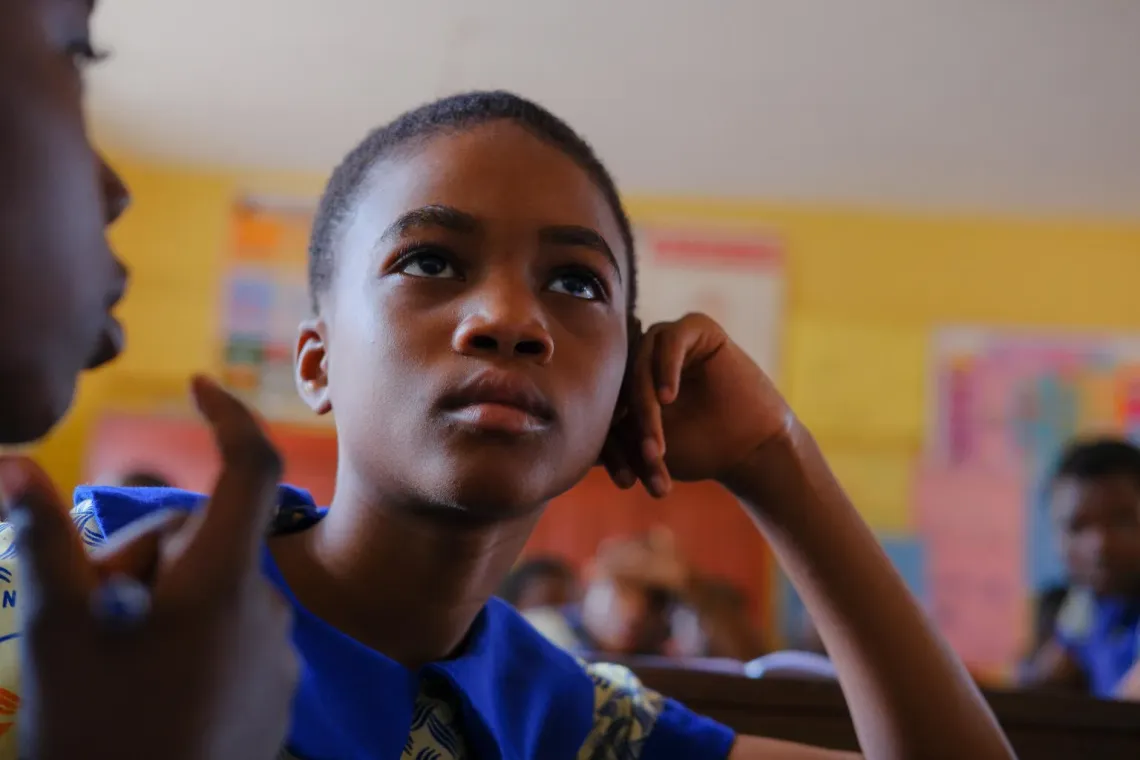A student pays attention to a session in class. The student is resting one hand on the cheek and leaning their elbow on a table 