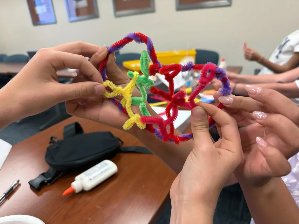 Multiple children's hands can be seen holding a model of future digital technology constructed using pipe cleaners