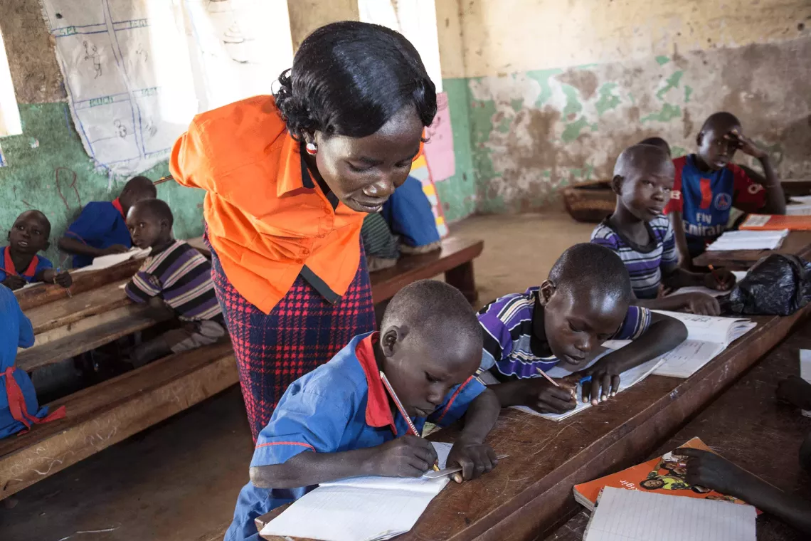 A teacher leans over to observe the work of children in a classroom