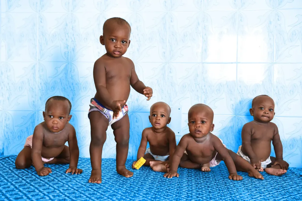 Five babies in a row, one standing and the other four sitting