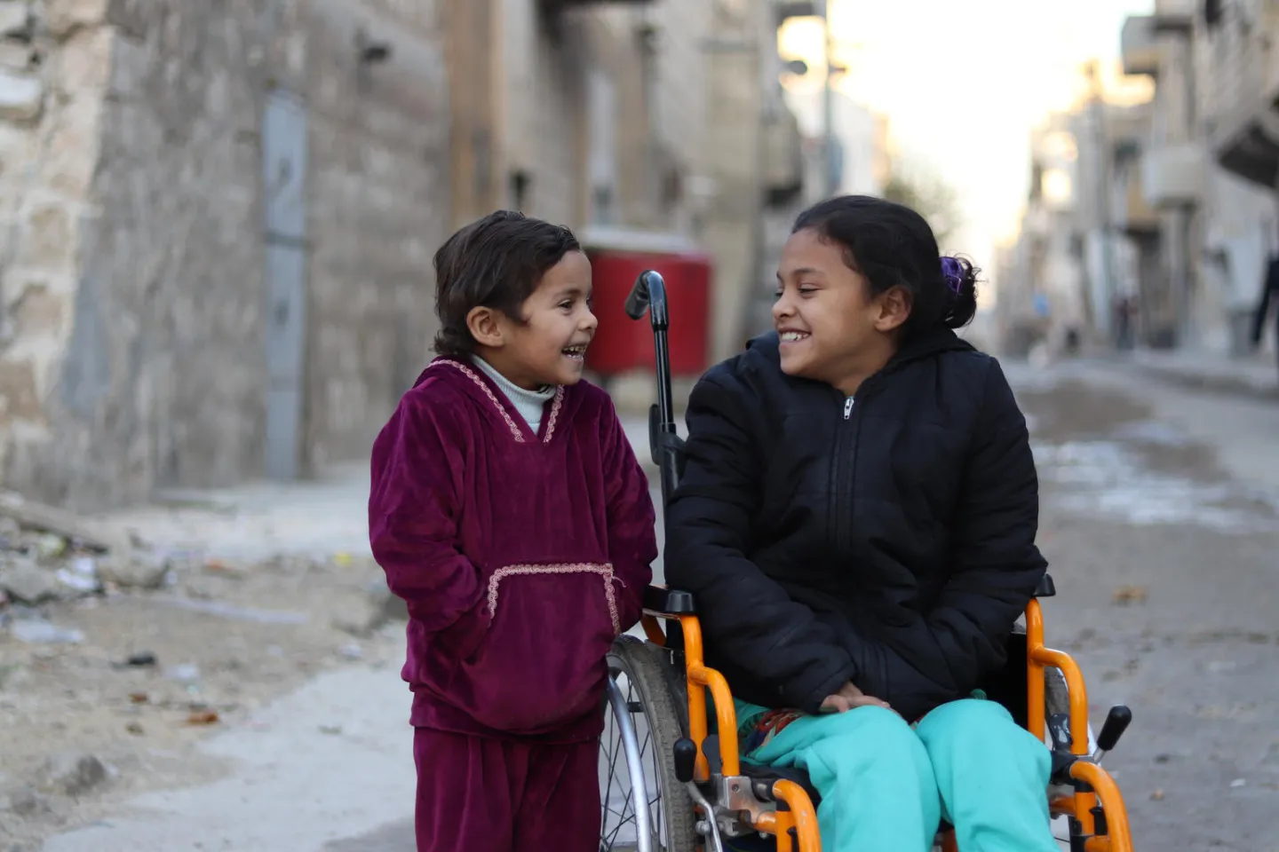 Hanaa, 8, who was paralysed by an exploding bomb and lost the use of her legs, sits in a wheelchair next to her sister Khadija, 5, near their home in Sakhoor neighborhood, east Aleppo city, Syrian Arab Republic.