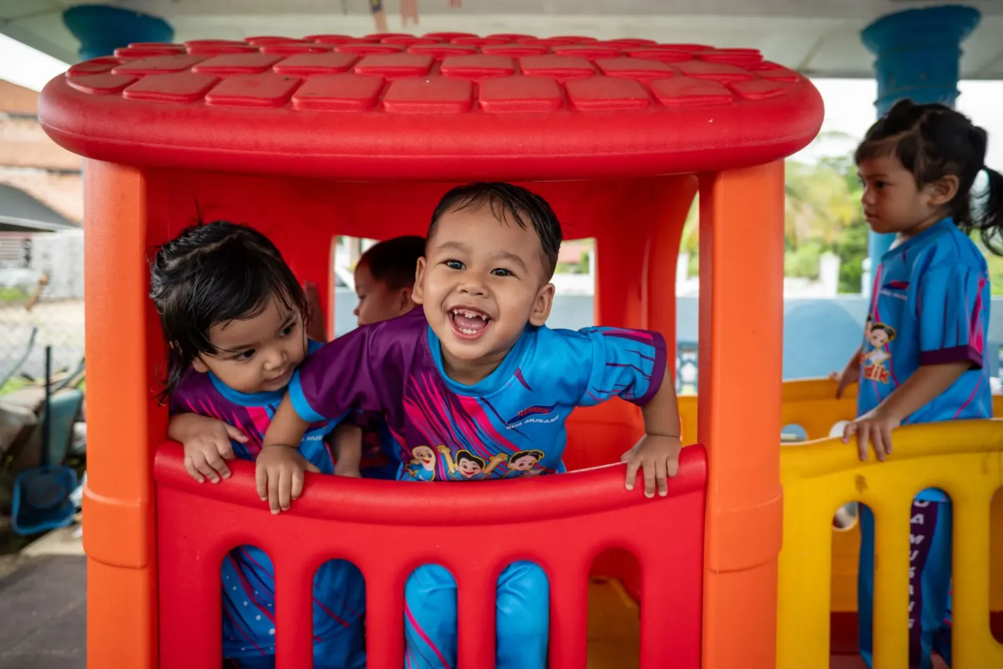 Young children laugh and play in a colourful playhouse at a childcare centre in Malaysia.