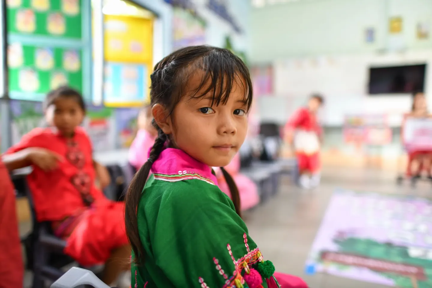 A girl in a green embroidered top looks over her shoulder in a school classroom in Thailand