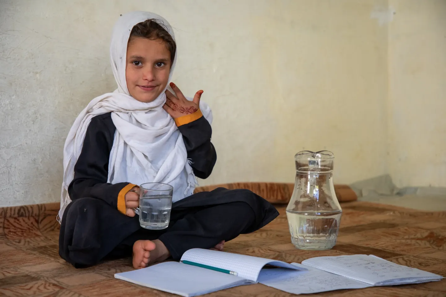 A girl smiles as she reads a book and drinks water from a glass