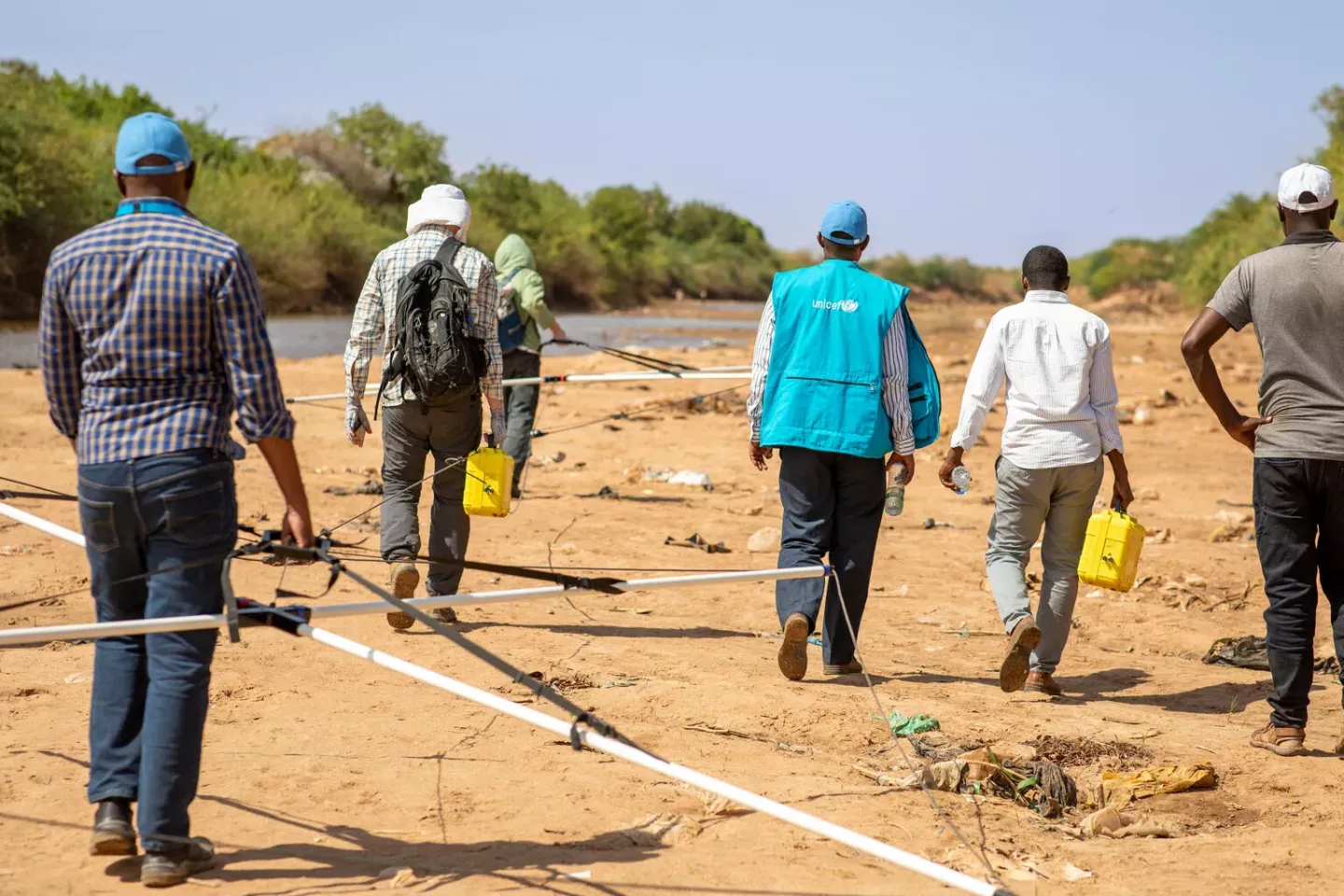 A team of men walk along a dry riverbank holding transient electromagnetics (TEM) equipment.