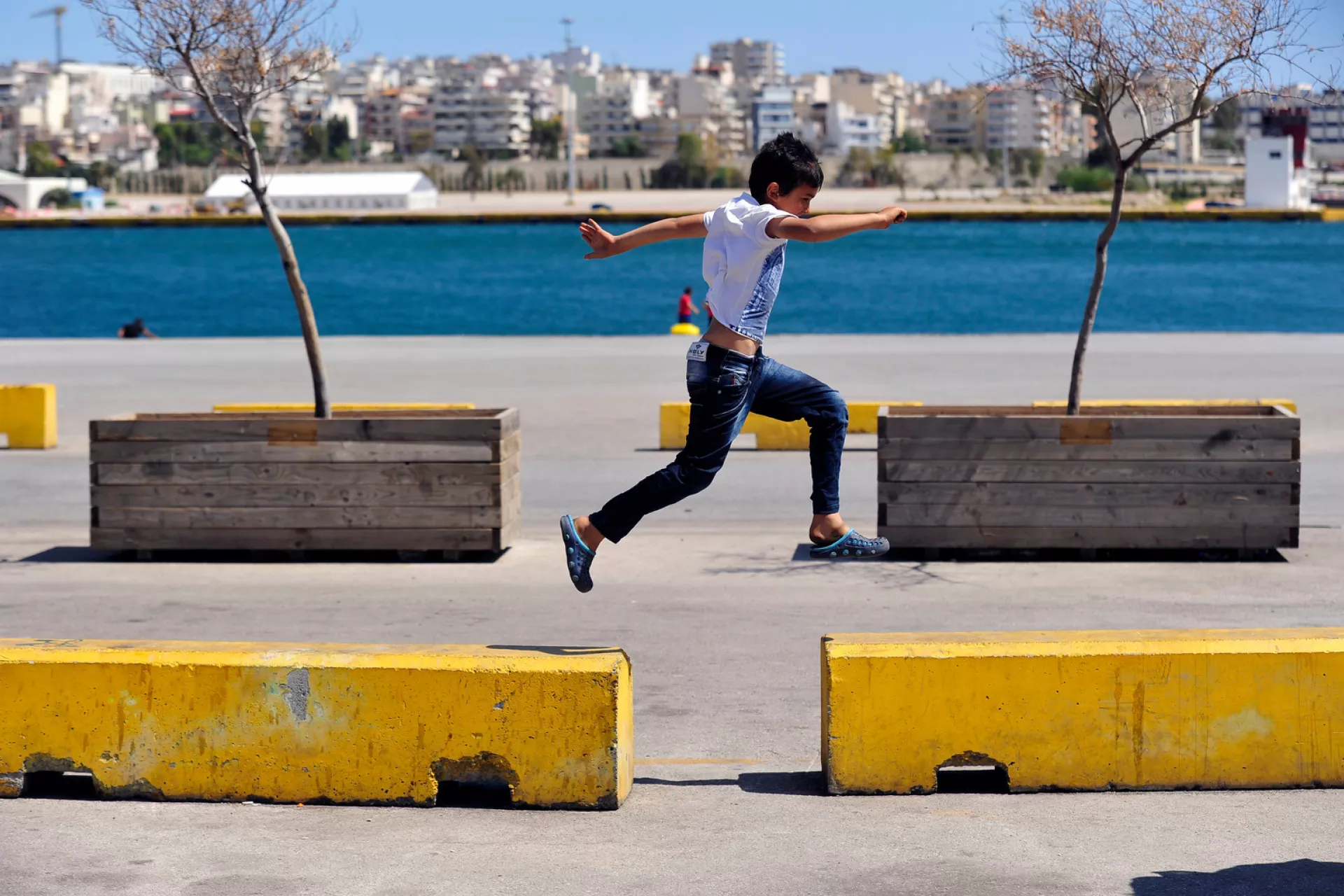 in Greece, Yousef, 11, from Syria jumps from barrier to barrier in the docks area of Piraeus, Greece&rsquo;s principal port.