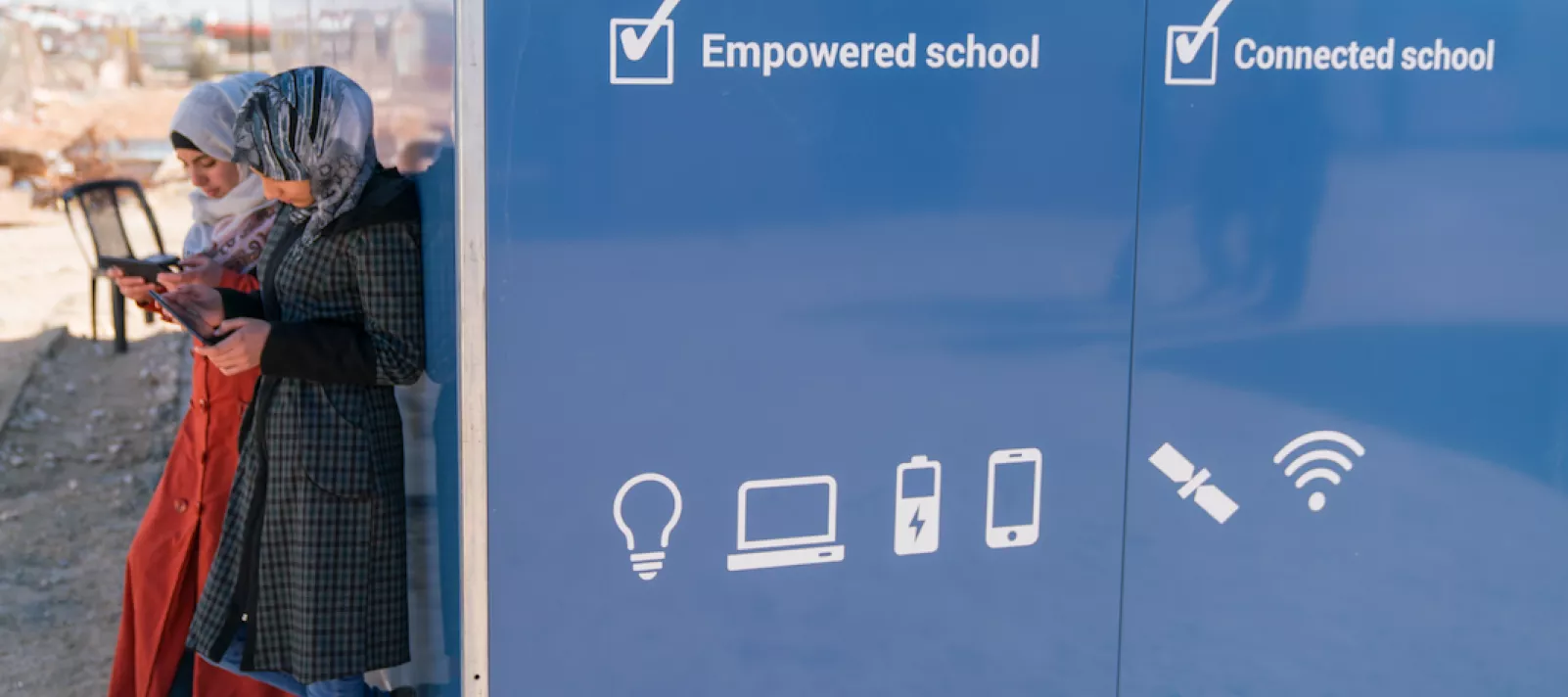 in Jordan, two adolescent girls use cellphones outside a solar kiosk in the Za&rsquo;atari camp for Syrian refugees