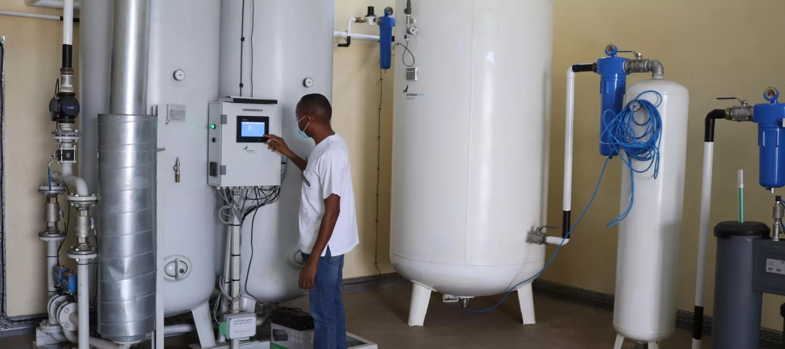 A man inspects an oxygen plant, which includes several large white oxygen tanks connected by pipes. 